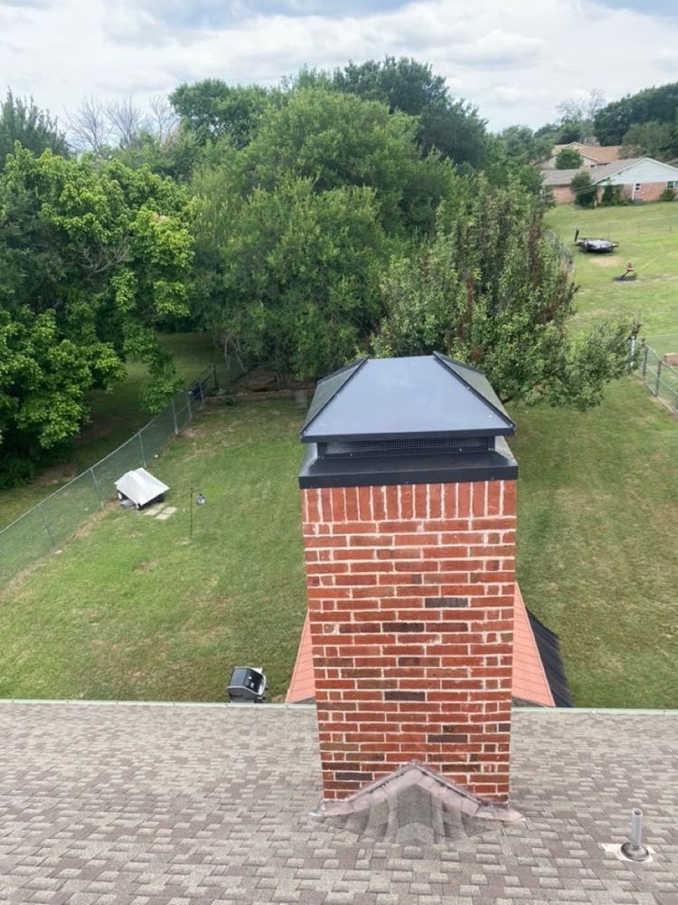 Aerial view of a red-brick chimney topped with a new black chimney cap in Dallas, TX